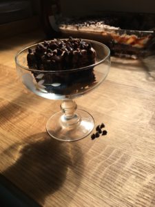 A piece of Bailey's Chocolate Poke Cake sitting in front of a cake pan with a slice missing from the cake.