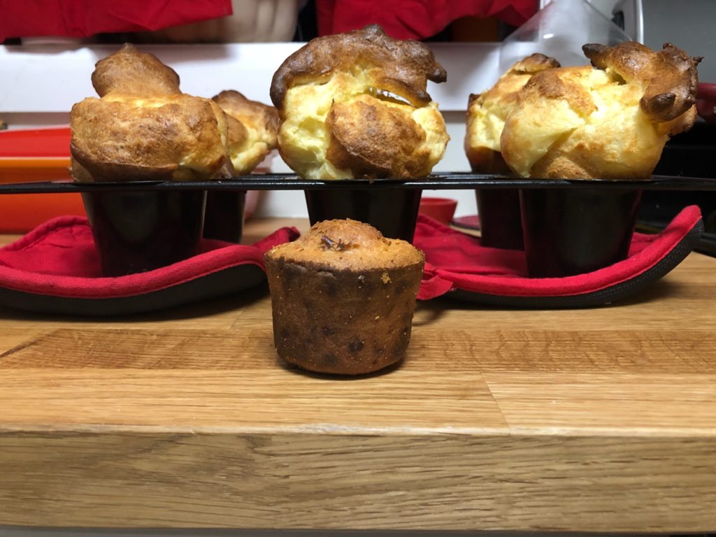 A deflated popover, more like a muffin, sitting in front of TOWERING, golden, amazing looking popovers.