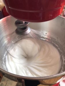 Egg whites are being whipped in a red Kitchenaid stand mixer.