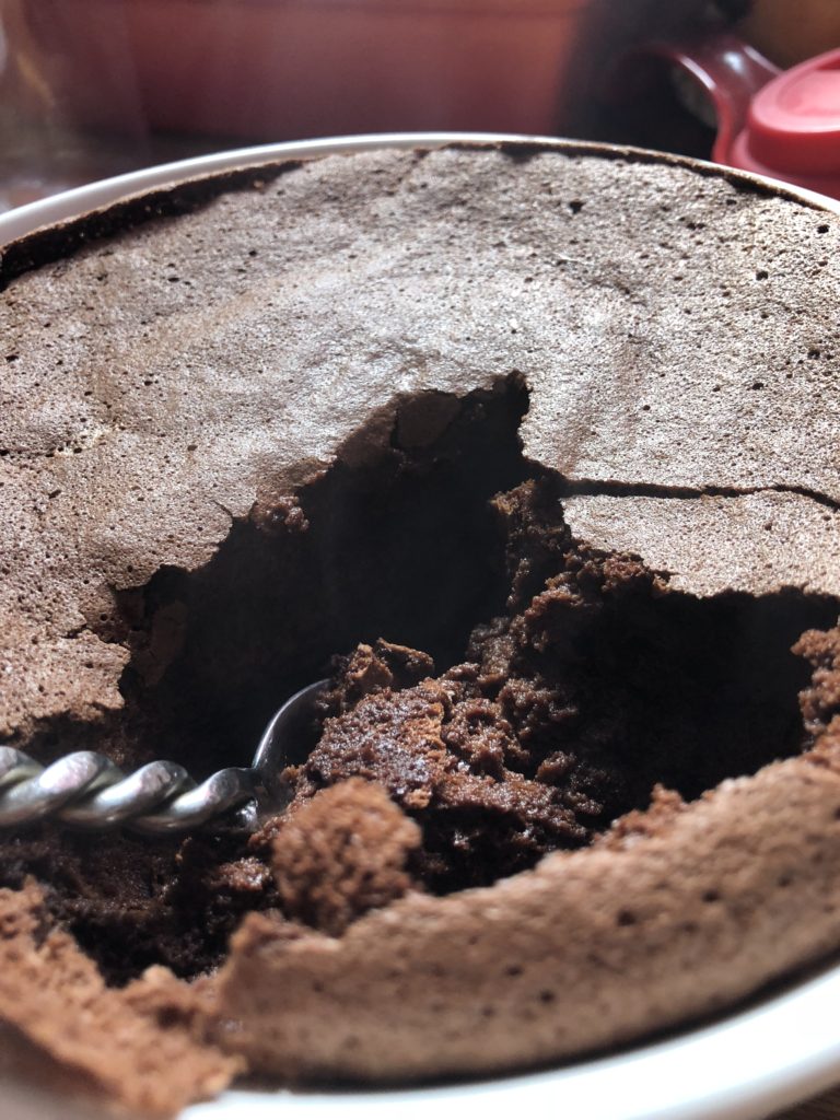 A very flat chocolate souffle with the crust cracked and a spoon sitting in it.
