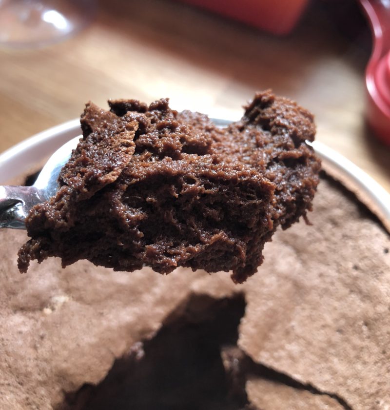 A spoonful of chocolate souffle with a very flat souffle behind it.